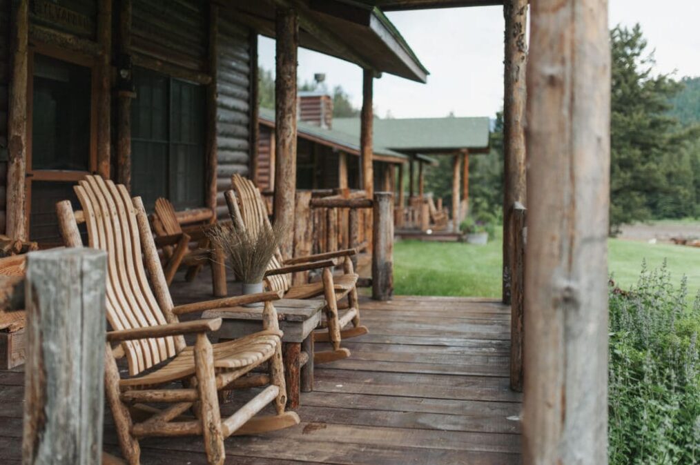 Rustic cabin porch with weathered wooden rocking chairs and a small table on a wooden deck.