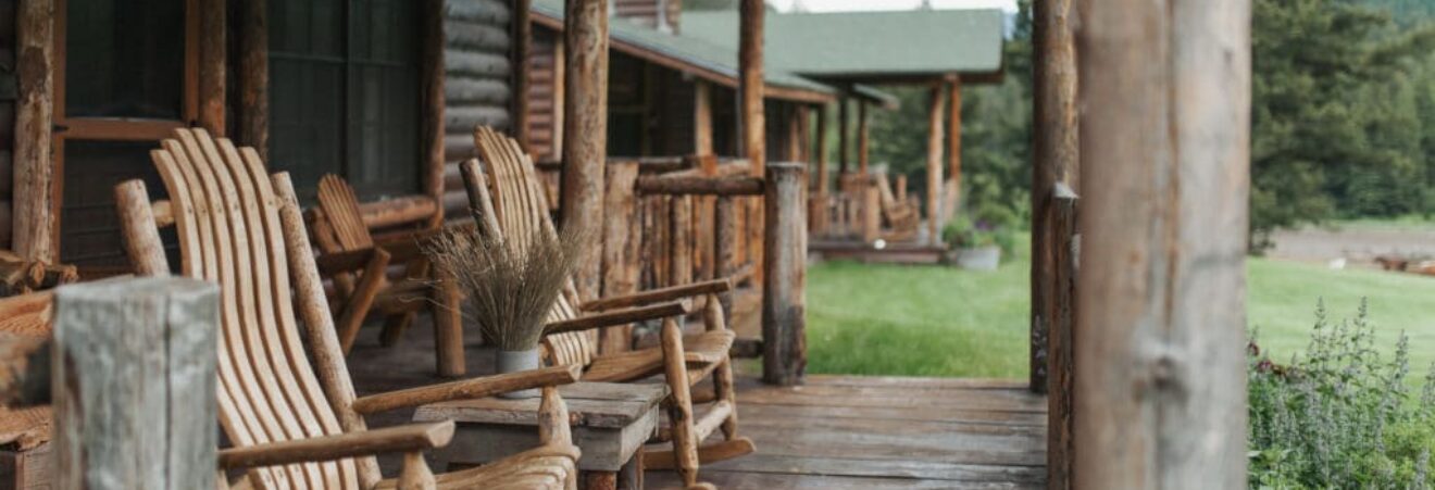 Rustic cabin porch with weathered wooden rocking chairs and a small table on a wooden deck.